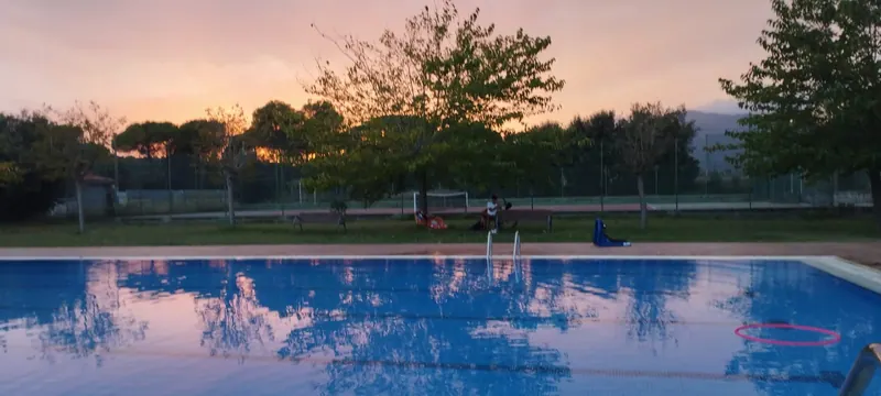 La gespa i la pista de tennis darrere la piscina, a última hora de la tarda.