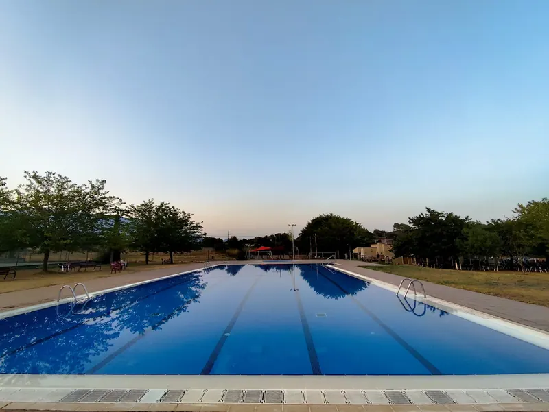 La piscina de Can Pagà al capvespre, amb els arbres reflectits a l'aigua.