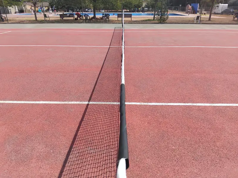 La xarxa de la pista de tennis vista arran de terra, amb la piscina al fons.